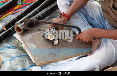 Einheimischer Handwerker schneidet Bambusstangen mit einer Säge, um bei einer Handwerkskarte in Kalkutta handwerkliche Artikel herzustellen Stockfoto