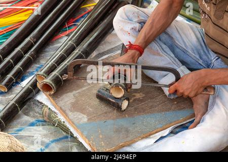 Einheimischer Handwerker schneidet Bambusstangen mit einer Säge, um bei einer Handwerkskarte in Kalkutta handwerkliche Artikel herzustellen Stockfoto