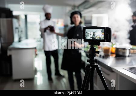 Nahaufnahme der Kamera, die Mitarbeiter der Lebensmittelindustrie bei der Zubereitung köstlicher Gourmet-Gerichte während der Übertragung aufzeichnet. Köche im Restaurant professionelle Küche Dreharbeiten Kochstunde für kulinarische Schule. Stockfoto