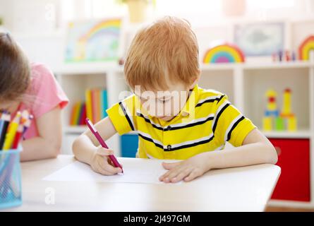 Schuljunge im Klassenzimmer sitzt an den Tischen und schreibt eine Lektion. Stockfoto