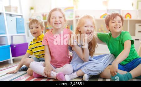 Eine Gruppe von Kindern, die drinnen auf dem Boden sitzen und in die Kamera schauen. Stockfoto