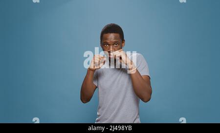 Aggressiver Mann, der Fäuste zusammenhält und erhöhte Knöchel an der Kamera zeigt, sich wütend fühlt und Luftanschläge verführt. Wütender gewalttätiger Schläger, der sich auf Kampf und Protest im Studio, Kampfdemonstration vorbereitet. Stockfoto