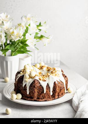 Karottenkuchen mit Frischkäse-Zuckerguss, Walnüsse und Osterdekor mit Blumen auf weißem Tisch. Speicherplatz kopieren. Stockfoto