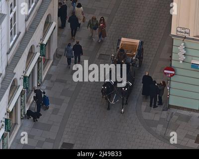 Luftaufnahme eines fiacre, einer vierrädrigen Pferdekutsche, mit Touristen, die in einer engen Straße im Zentrum von Wien, Österreich, Menschen passieren. Stockfoto