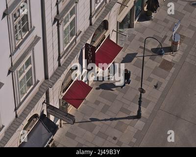 Luftaufnahme von Menschen, die an einem Vinothek-Laden mit rot gefärbter Markise im historischen Zentrum von Wien, Österreich, vorbeikommen, an sonnigen Tagen. Stockfoto