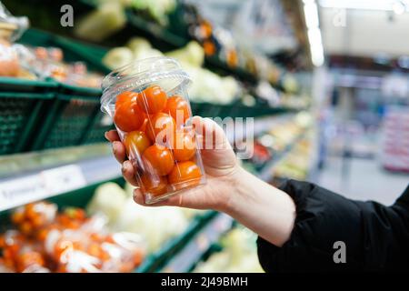 Eine Kundin wählt im Geschäft Kirschtomaten aus. Nahaufnahme. Stockfoto