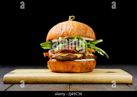 Leckerer Rindfleischburger mit Speck auf einem hölzernen Servierbrett Stockfoto