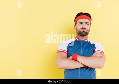 Nachdenklicher Sportler, der Arme auf Gelb isoliert kreuzt Stockfoto