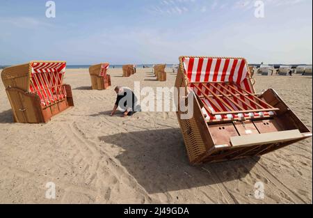 13. April 2022, Schleswig-Holstein, Travemünde: Ein Mitarbeiter eines Liegestuhlvermieters misst mit einer Klappregel den Abstand zwischen den Liegen, die er am Strand vor der Promenade von Travemünde aufstellt. Foto: Christian Charisius/dpa Stockfoto