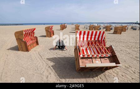 13. April 2022, Schleswig-Holstein, Travemünde: Ein Mitarbeiter eines Liegestuhlvermieters misst mit einer Klappregel den Abstand zwischen den Liegen, die er am Strand vor der Promenade von Travemünde aufstellt. Foto: Christian Charisius/dpa Stockfoto