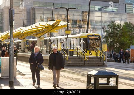 2. November 2018: Manchester, Großbritannien - Metrolink-Straßenbahnhaltestelle am Exchange Square, Seniorenpaar zu Fuß, Wintersonne. Stockfoto