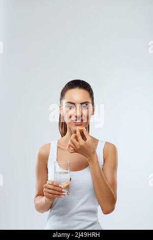 Glückliche lächelnde Frau, die Pille mit Cod Liver Oil Omega-3 und ein Glas frisches Wasser am Morgen hält. Vitamin D, E, A Fischöl Kapseln. Ernährung. Mutter Stockfoto