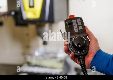 Worker hält das Drehbedienfeld für die Genauigkeitseinstellung der cnc-Bearbeitungszentrum-Maschine. Stockfoto