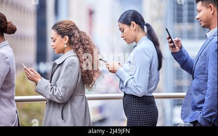 Was es sonst noch in langen Warteschlangen zu tun gibt. Aufnahme einer Gruppe von Geschäftsleuten in einer Schlange bei der Arbeit. Stockfoto