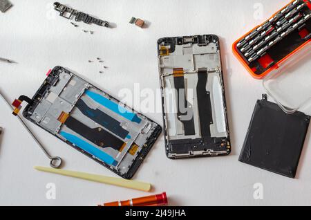 Repair of smartphones concept. Hand tool and disassembled phone lying on the table. Part of a series. Indoors. Selective focus. Stockfoto