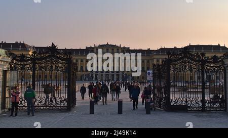 Vorderansicht des Eingangstors zum berühmten Schloss Schönbrunn in Wien, Österreich bei nachmittäglicher Sonneneinstrahlung mit Menschen, die den Park betreten und verlassen. Stockfoto