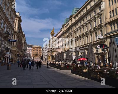 Blick auf die geschäftige Einkaufsstraße Graben im historischen Zentrum von Wien, Österreich an sonnigen Tagen mit Pestsäule (Trinity Column), Café und Menschen. Stockfoto