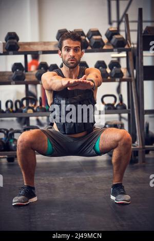 Bleiben in Spitzenform. Eine kurze Aufnahme eines hübschen jungen Mannes, der beim Training im Fitnessstudio hockt. Stockfoto