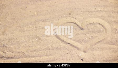 Herz in den Sand gezogen. Strand Hintergrund. Draufsicht. Selektiver Fokus Stockfoto