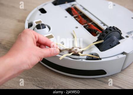 Eine Frau entfernt Haare aus der Bürste eines Roboter-Staubsaugers. Das Konzept eines Roboter-Staubsaugers reinigt die Böden im Haus. Stockfoto