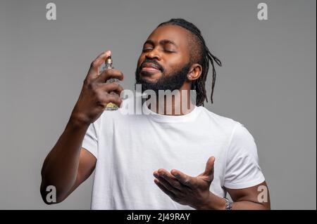 Heiterer afroamerikanischer Kerl, der sich mit köln spritzing Stockfoto