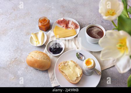 Frühstück mit herzhaften und süßen Zutaten, Brötchen, Ei, Kaffee und Blumen auf hellem Steingrund, Kopierraum, Blick von oben, ausgewählter Fokus, Stockfoto