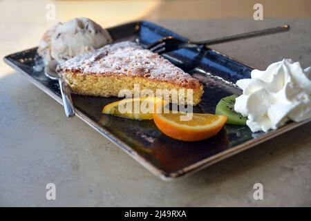 Mandelkuchen mit Eis und Früchten auf schwarzem Teller und Marmortisch, köstliches Dessert aus Spanien, Kopierraum, ausgewählter Fokus, enge Fie-Tiefe Stockfoto