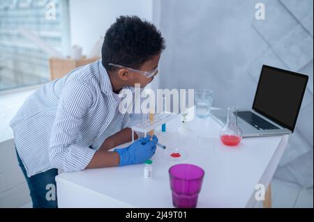 Ein dunkelhaariger Junge in einem Labormantel, der während eines chemischen Experiments beschäftigt aussieht Stockfoto