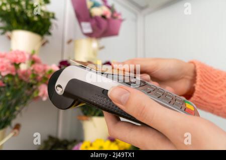 Nahaufnahme eines Zahlungsterminals in den Händen eines Floristen, wobei die Hand eines Kunden eine Bestellung mit einer kontaktlosen Karte bezahlt Stockfoto