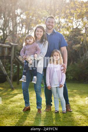 Familie ist alles. Ganzkörperportrait einer liebevollen jungen vierköpfigen Familie, die zu Hause im Garten posiert. Stockfoto