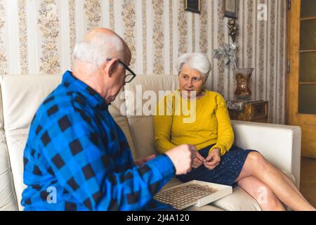 Ältere kaukasische heterosexuelle Paare auf Ledersofa lösen Puzzle in ihrer Vintage-Wohnung. Aktive Senioren. Hochwertige Fotos Stockfoto
