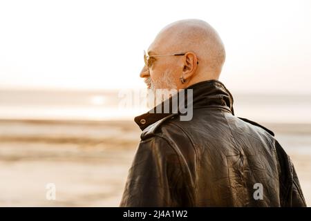 Auffälliger älterer Mann in Lederjacke, der am Sommertag im Freien zur Seite schaut Stockfoto