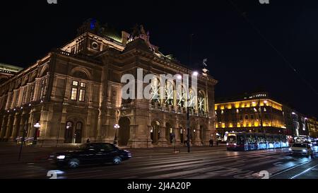 Vorderansicht des Haupteingangs der berühmten Wiener Staatsoper, Österreich, in der historischen Innenstadt mit beleuchteter Steinfassade. Verschwommene Bewegung. Stockfoto