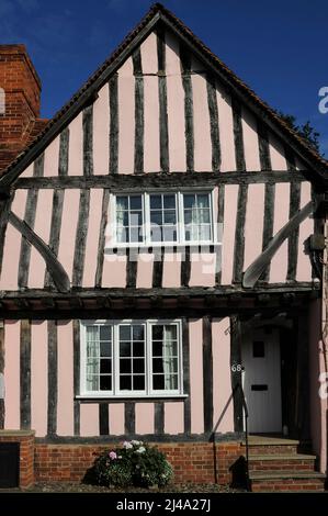 Ein Tudor-Haus mit Holzrahmen in Lavenham, Suffolk, England, eine alte Stadt aus Wolle und Stoff. Dieses Haus in der Church Street 68 wurde in den 1500s Jahren gebaut. Er verfügt über einen breiten Giebel im ersten Stock und ein oberes Stockwerk, das von einem Steg mit freiliegenden Trägern gestützt wird. Putz in Rosa füllt die Lücken zwischen Eichenholzstücken an der Fassade. Stockfoto