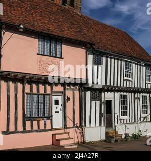 TUDOR Holzrahmenhäuser, erbaut in den späten 1400s oder frühen 1500s Jahren, 85 und 86 Church Street, Lavenham, Suffolk, England. Über der Tür zur Nummer 85, Staddles Cottage (das rosa Haus auf der linken Seite), ist eine Reihe von Blumenverzierungen, die aus dem späten 1600er. Jahrhundert stammen, als das ursprüngliche Anwesen in zwei Hütten aufgeteilt wurde. Pargetting oder Pargeting ist eine traditionelle Methode, dekoratives Design zu schaffen, indem Druck auf nassen Putz ausgeübt wird, insbesondere im Zusammenhang mit den East Anglian Counties Norfolk, Suffolk und Cambridgeshire. Stockfoto