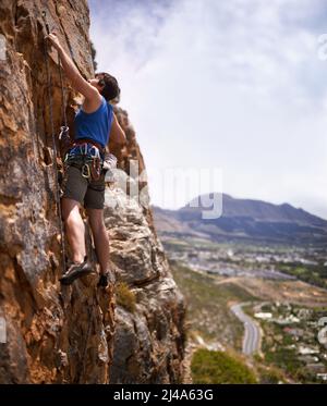 Mutiger Bleibergsteiger. Aufnahme einer jungen Frau, die beim Klettern einen Bolzen einknipst. Stockfoto