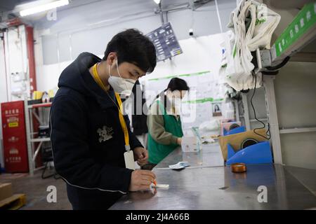 (220413) -- SHANGHAI, 13. April 2022 (Xinhua) -- der Supervisor Wu Renhua (L) und ein Mitarbeiter führen schnelle Antigen-Tests in der Outlet-Abteilung von Meituan Maicai im ostchinesischen Shanghai durch, 12. April 2022. Mehr als 30 Mitarbeiter der Online-Lebensmittelplattform Meituan Maicai, die in der Outlet-Abteilung an der Yixian Road in Shanghai leben und arbeiten, haben sich mit der Vorbereitung von Vorräten für die Bewohner beschäftigt. Sie sind damit beschäftigt, die bestellten Lebensmittel zu sortieren und zu verpacken, bevor die Artikel von Kurierern an die Kunden geliefert werden. Während des jüngsten Wiederauflebens der Epidemie durchschnittlich mehr als 3.000 Stockfoto