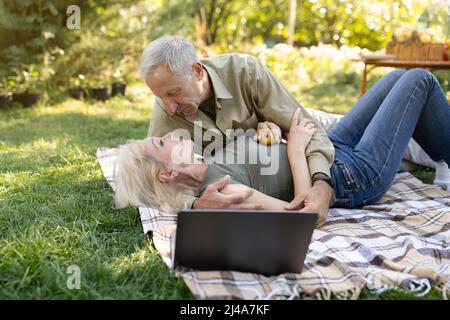 Zartes verheiratetes Seniorenpaar genießt Zeit zusammen, verbringt einen Tag im Freien in ihrem Garten und macht ein Picknick auf dem Rasen Stockfoto