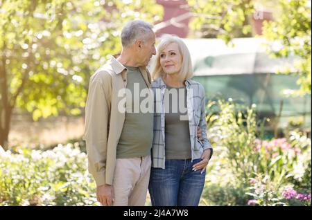 Liebe und Romantik im Seniorenalter Konzept. Liebevolle ältere Ehepartner, die sich in ihrem Garten umarmen und lächeln Stockfoto