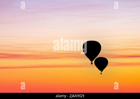 Ein Paar Heißluftballons werden in einem zusammengesetzten Bild vor einem farbenfrohen Sonnenuntergang silhouettiert. Stockfoto