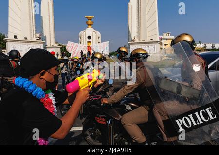 Bangkok, Thailand. 13. April 2022. Ein Protestler sah während der Demonstration Wasser auf Polizeistreitkräfte schießen. Prodemokratische Demonstranten versammelten sich am Demokratie-Denkmal zum Thema des Songkran-Festivals und nahmen an Wasserkämpfen Teil, wobei sie sich gegen die Politik der Regierung COVID-19 verstießen, die in diesem Jahr Wasserkämpfe verboten hatte. Demonstranten marschierten auch entlang der Ratchadamnoen-Straße und forderten eine Reformation der Monarchie. Kredit: SOPA Images Limited/Alamy Live Nachrichten Stockfoto