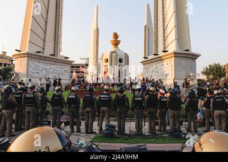 Bangkok, Thailand. 13. April 2022. Die Demonstranten grüßt mit drei Fingern, während die Polizei während der Demonstration am Demokratiedenkmal auf der Wache steht. Prodemokratische Demonstranten versammelten sich am Demokratie-Denkmal zum Thema des Songkran-Festivals und nahmen an Wasserkämpfen Teil, wobei sie sich gegen die Politik der Regierung COVID-19 verstießen, die in diesem Jahr Wasserkämpfe verboten hatte. Demonstranten marschierten auch entlang der Ratchadamnoen-Straße und forderten eine Reformation der Monarchie. Kredit: SOPA Images Limited/Alamy Live Nachrichten Stockfoto