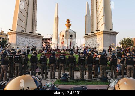 Bangkok, Thailand. 13. April 2022. Die Demonstranten grüßt mit drei Fingern, während die Polizei während der Demonstration am Demokratiedenkmal auf der Wache steht. Prodemokratische Demonstranten versammelten sich am Demokratie-Denkmal zum Thema des Songkran-Festivals und nahmen an Wasserkämpfen Teil, wobei sie sich gegen die Politik der Regierung COVID-19 verstießen, die in diesem Jahr Wasserkämpfe verboten hatte. Demonstranten marschierten auch entlang der Ratchadamnoen-Straße und forderten eine Reformation der Monarchie. (Foto von Varuth Pongsapipatt/SOPA Image/Sipa USA) Quelle: SIPA USA/Alamy Live News Stockfoto