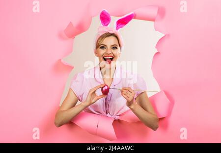 Ostertag. Glückliche Frau in Hasenohren, die durch Papier guckt. Lächelnde Kaninchen Frau malen Ei. Stockfoto