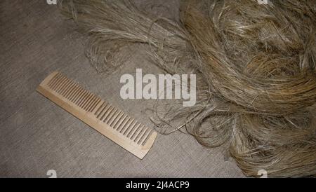 Leinenfasern auf einem Hintergrund aus Leinenstoff. Holzkamm zum Kämmen von Flachs. Das Anbauen, Kämmen und Spinnen von Flachs zu Hause ist eine alte Handarbeit. Anlage. Stockfoto