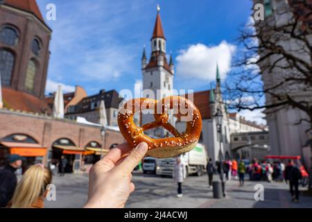 Hält eine brezel im Bayern-Stil auf dem Markt für Lebensmittel mit Hintergrund des alten rathauses in münchen. Stockfoto