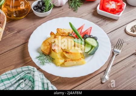 Hausgemachte, appetitlich gebackene Kartoffeln mit Gemüse auf einem weißen Teller auf einem dunklen Holzhintergrund. Stockfoto