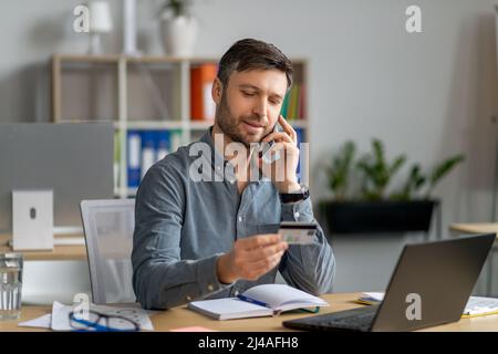 Einfaches Zahlungskonzept. Reifer Geschäftsmann, der mit Kreditkarte arbeitet und mit dem Kundenservice über das Mobiltelefon spricht Stockfoto
