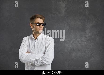 Selbstbewusster junger Mann in einer Strolch-Lebensbrille, der vor grauem Hintergrund des Kopierraums steht Stockfoto