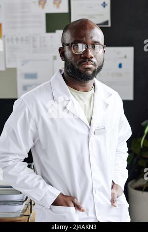 Porträt eines afrikanischen Spezialisten für Brillen und Laborkittel, der im Büro steht und auf die Kamera schaut Stockfoto